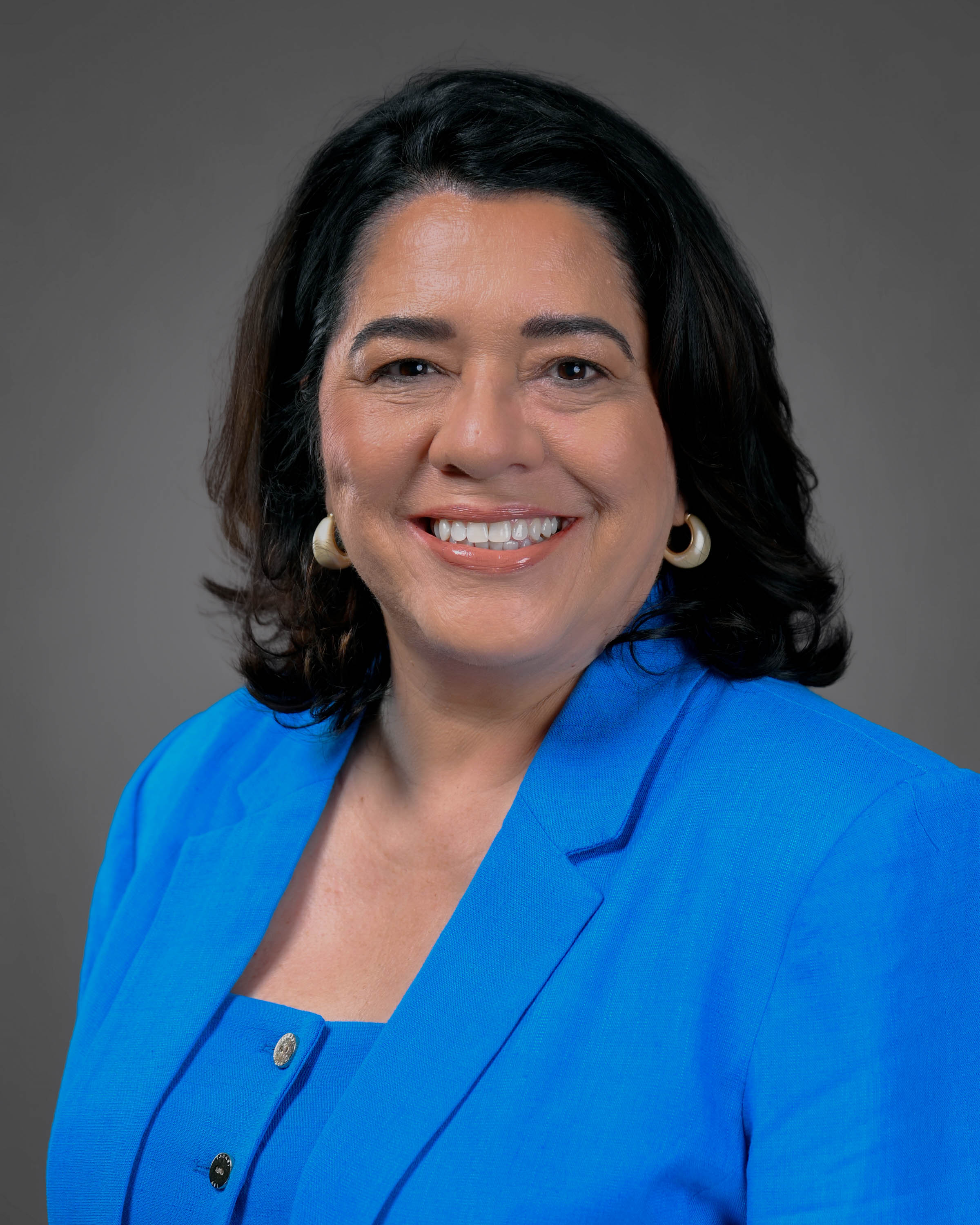 Smiling woman with dark should length hair wearing a blue jacket and top on.